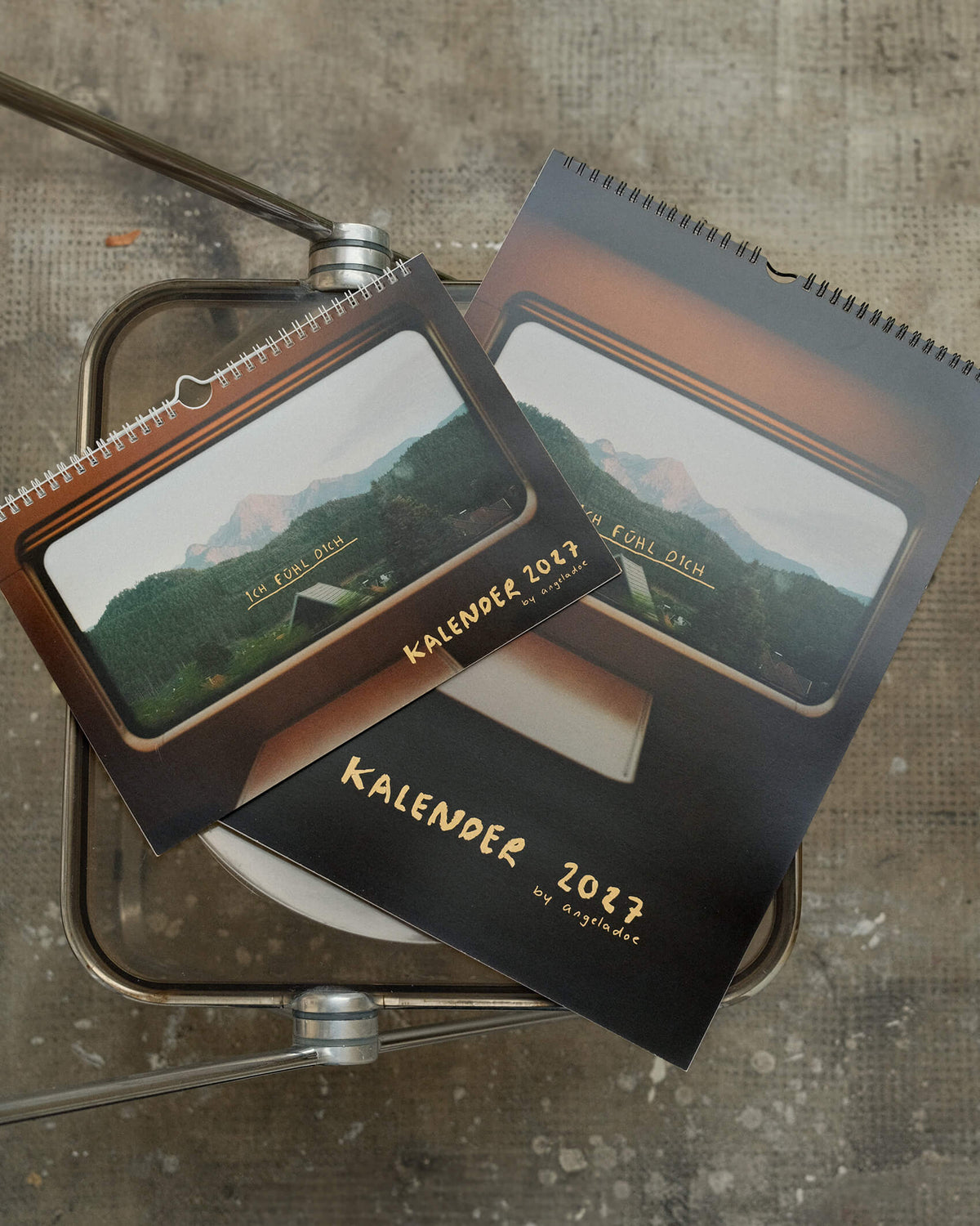 Titelblatt des Sprüchekalenders 2027 „Ich fühl dich“ von Angela Doe: Blick durch ein Zugfenster auf Wälder und Berge mit gelber handgeschriebener Schrift.