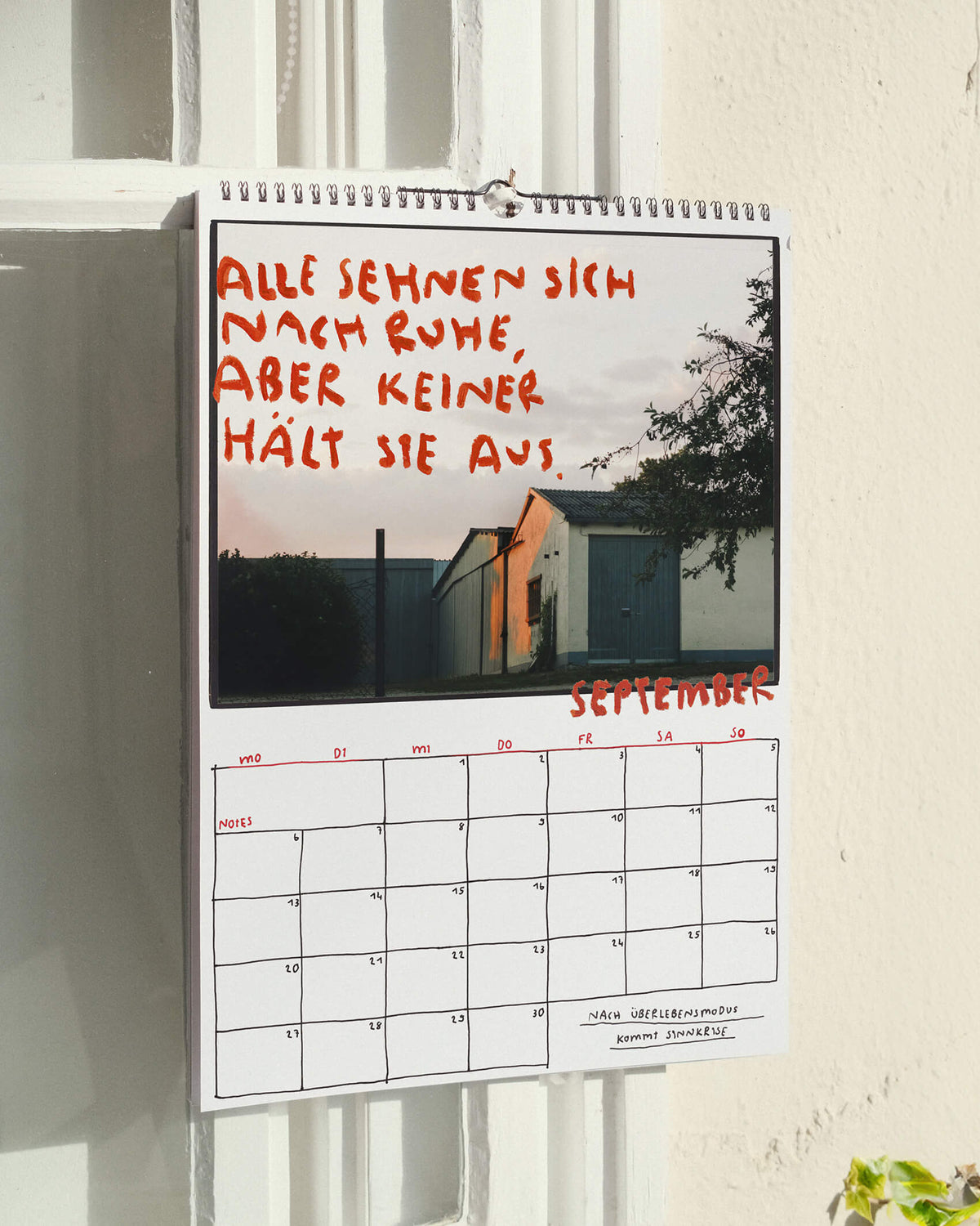 Septemberblatt des Sprüchekalenders 2027 von Angela Doe: Gebäude im Abendlicht mit dem Spruch „Alle sehnen sich nach Ruhe, aber keiner hält sie aus.“